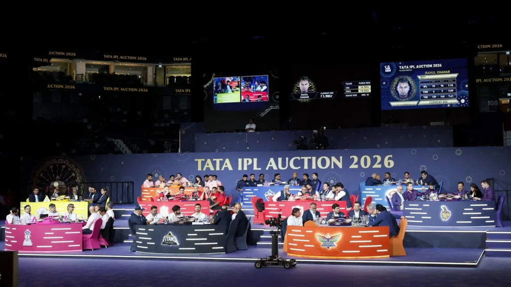 IPL 2026 mega auction hall with franchise tables and player bidding screen on stage.
